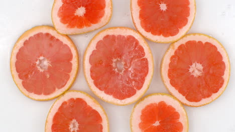 Top-view:-on-a-white-background-a-many-fresh-grapefruit-is-lying-in-the-water-water-drops-are-falling-from-above-and-splashes-are-falling-in-slow-motion-in-all-directions.